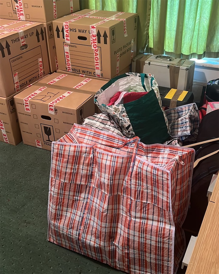 Moving boxes and checked laundry bags packed in a bedroom, ready for the van